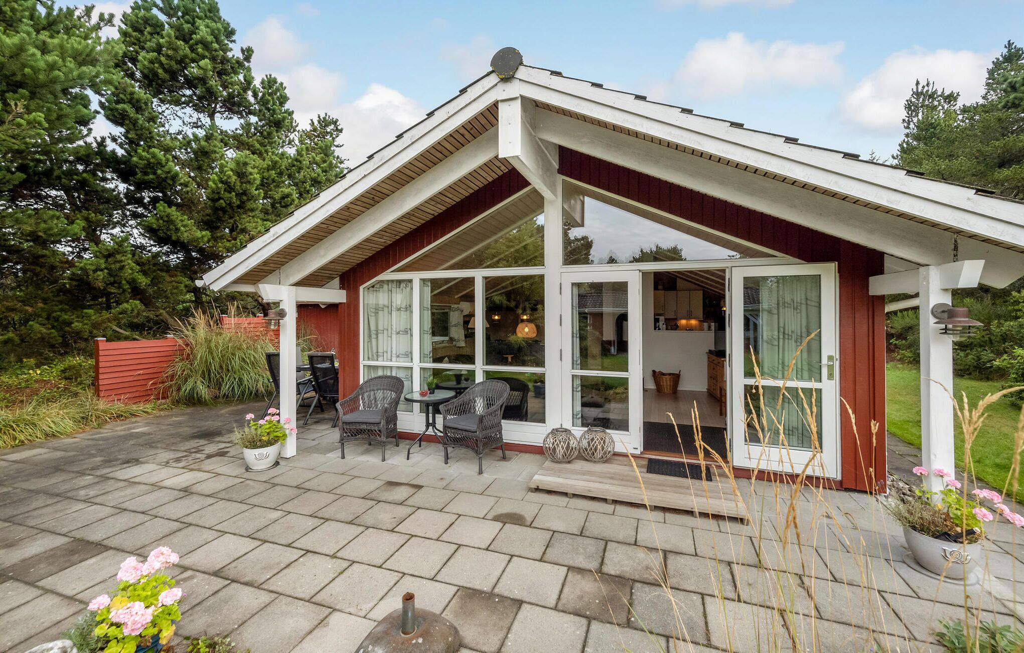 Une maison dotée d’un patio couvert, d’un coin repas avec des chaises et offrant une vue sur l’intérieur grâce à de grandes fenêtres.