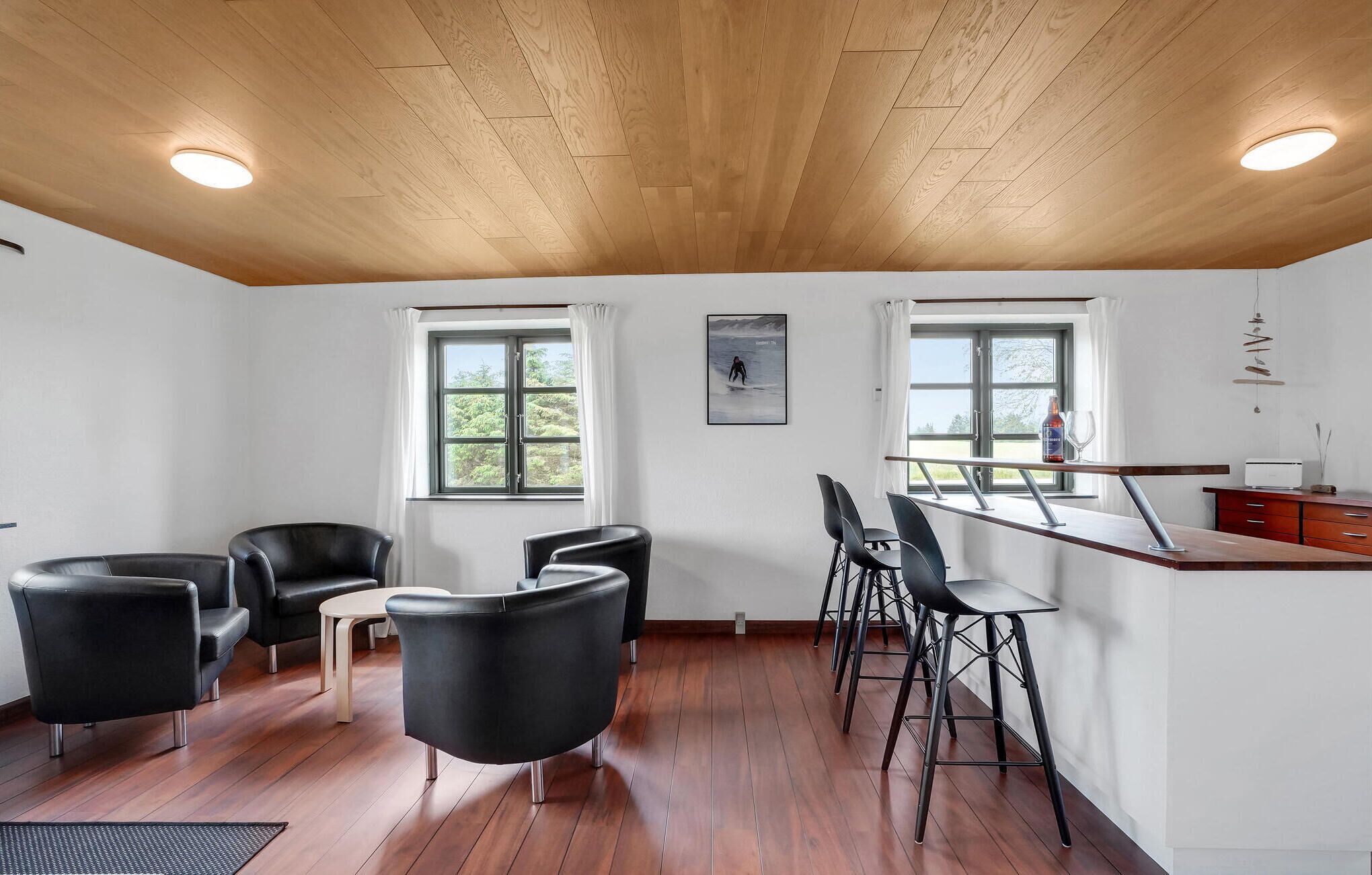 Un intérieur moderne avec un plafond en bois, un coin repas doté de tabourets de bar et deux fenêtres avec des rideaux.