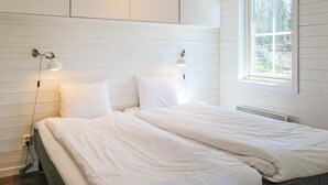 Ein Schlafzimmer mit einem Bett, weißer Bettwäsche, zwei Wandleuchten und einem Fenster mit Blick auf Bäume.