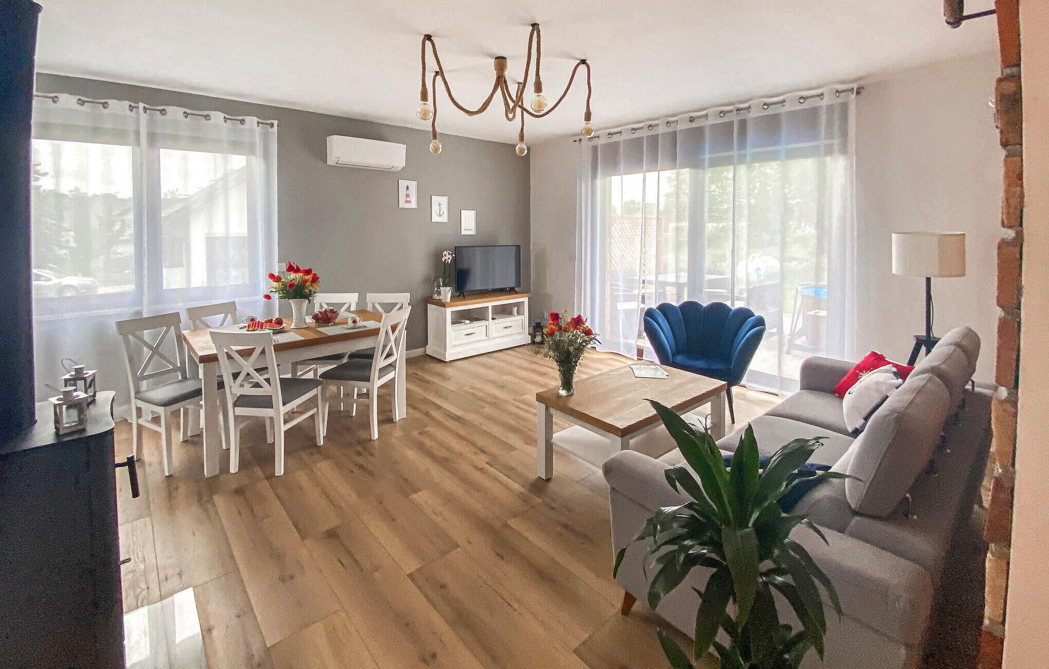 Uma sala de estar com piso de madeira, móveis brancos, uma TV e um lustre.