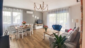 A living room with a wooden floor, white furniture, a TV, and a chandelier.