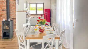A dining area with a wooden table set for four, white chairs, a red refrigerator, and a brick wall.