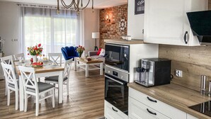 A modern kitchen with white cabinetry, a built-in oven, a coffee maker, and a brick accent wall.