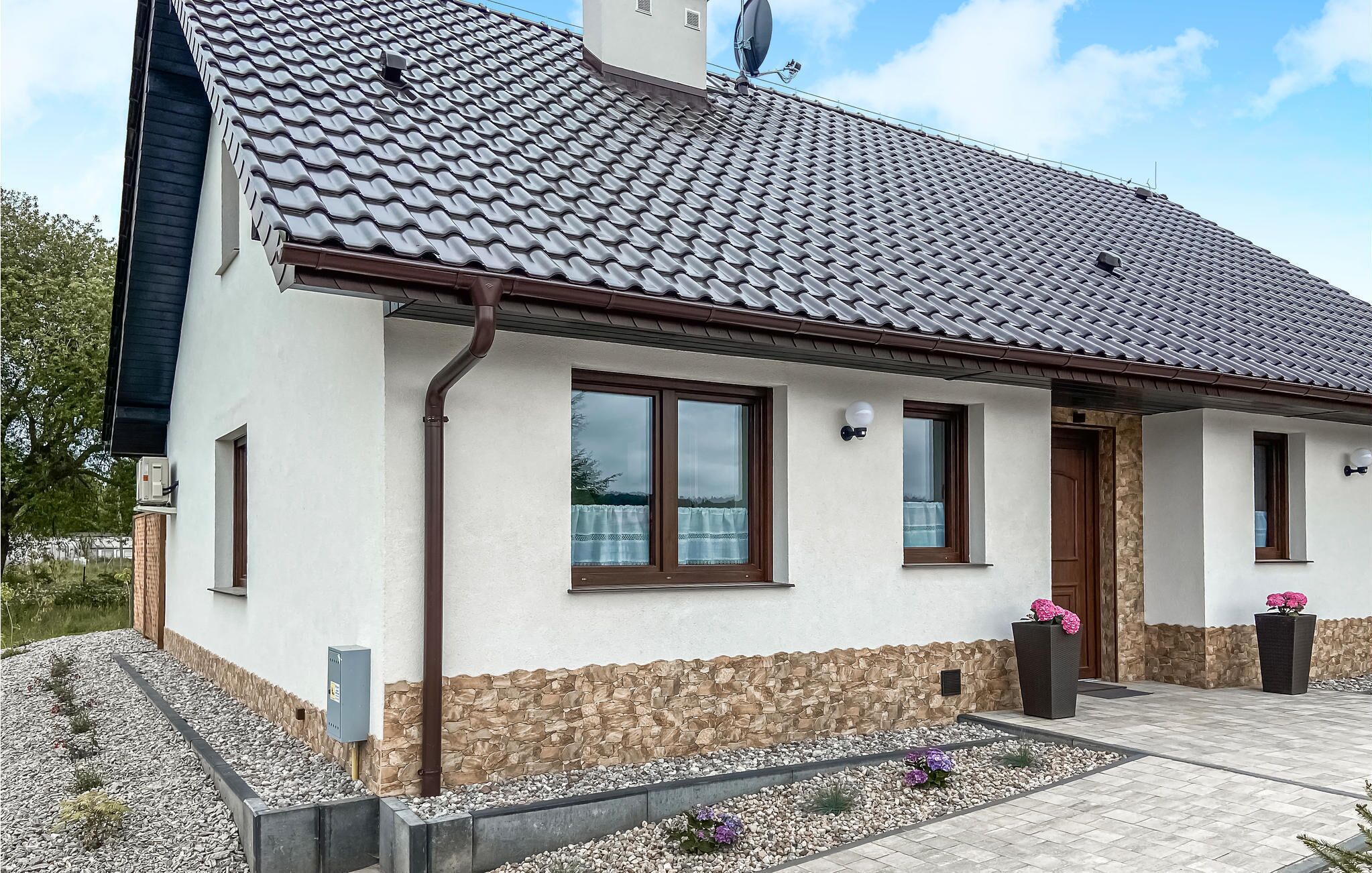 Una casa moderna con techo de tejas, base de piedra y un pequeño jardín con flores.