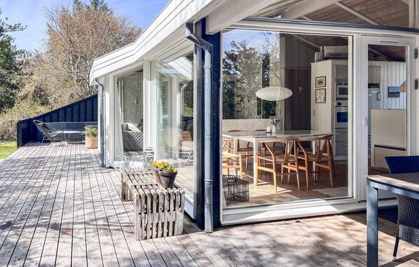 Een moderne woning met een terras, een eethoek met tafel en stoelen, en een keuken die zichtbaar is door glazen deuren.