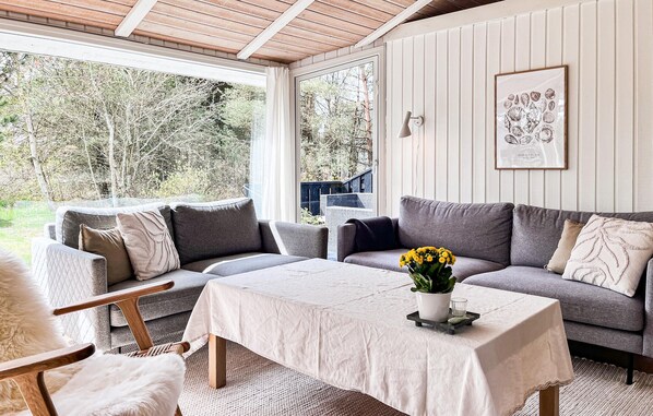 A cozy room with a grey sofa, a small table with a vase of flowers, and a framed picture on the wall.