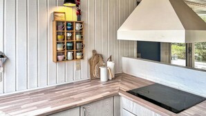 Una cocina con encimera de madera, estante empotrado con tazas, una tetera y una ventana con vistas.