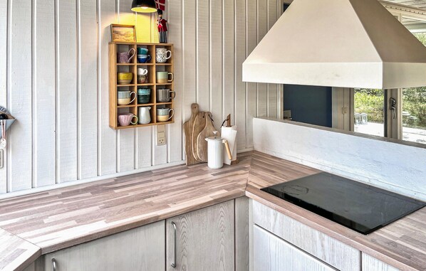 A kitchen with a wooden countertop, a built-in shelf with mugs, a kettle, and a window with a view.