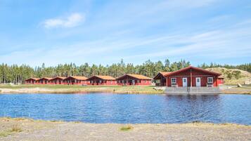 Une rangée de cabanes rouges au bord d’un lac, avec une forêt en arrière-plan.