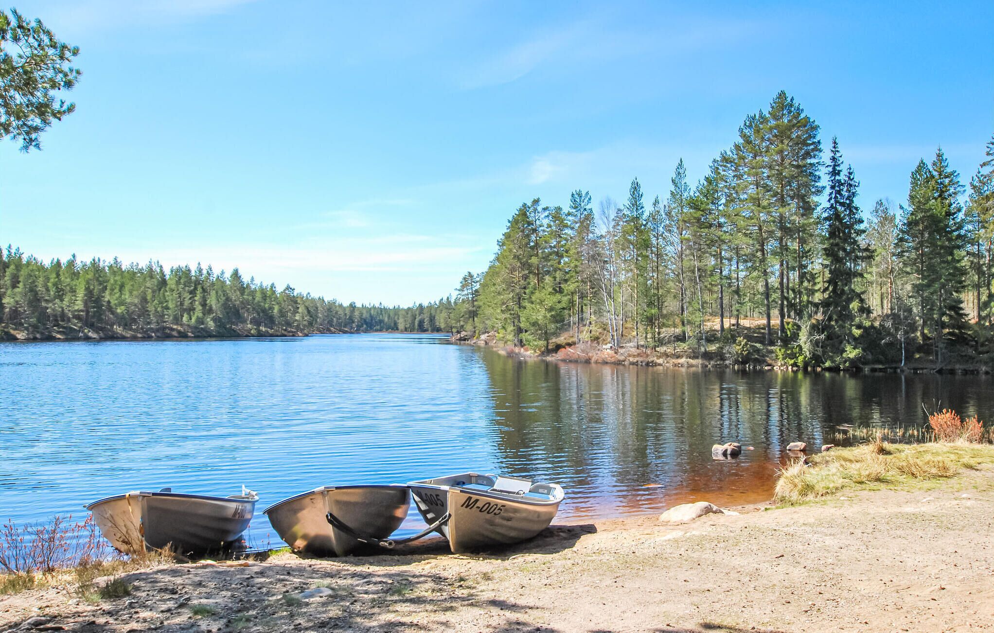 A calm lake with two boats on the shore, surrounded by dense forest.