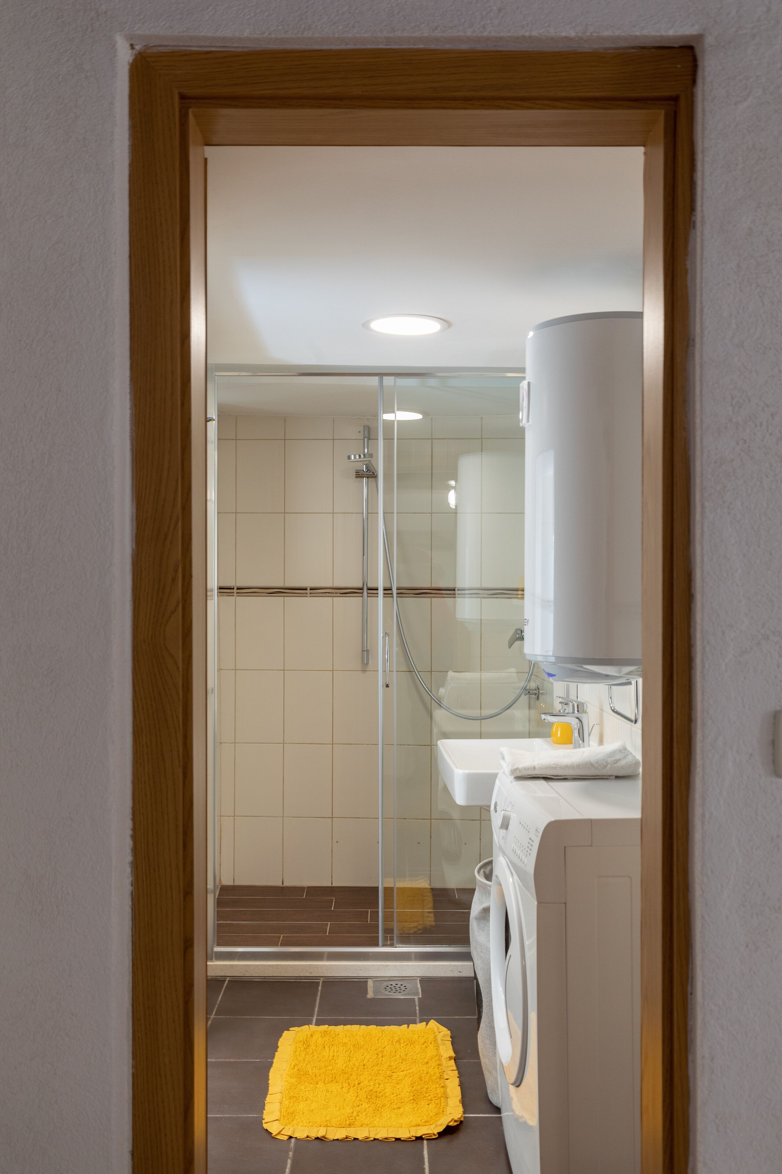 Un baño con cabina de ducha de vidrio, lavadora y lavamanos.
