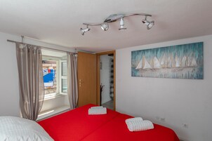 Quarto de hotel com colcha vermelha, toalhas brancas, quadro de barcos à vela e luminária no teto.
