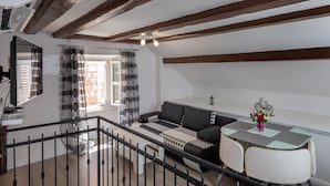 A modern loft bedroom with exposed wooden beams, a black and white sofa, a dining table, and a view of the city through a window. - Old Town Charming Nest (Dubrovnik)