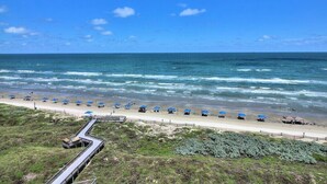 A beach with a wooden boardwalk leading to the shore, lined with blue umbrellas and beach chairs. - Sea Gull #908: Beachfront 2 Bedroom 2 Bathroom With Spectacular Views and 24 Hour Management (Port Aransas)