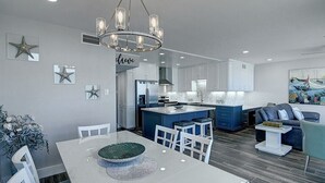 A modern kitchen with white cabinets, a central island, and a dining area with a white table and chairs. - Sea Gull #908: Beachfront 2 Bedroom 2 Bathroom With Spectacular Views and 24 Hour Management (Port Aransas)