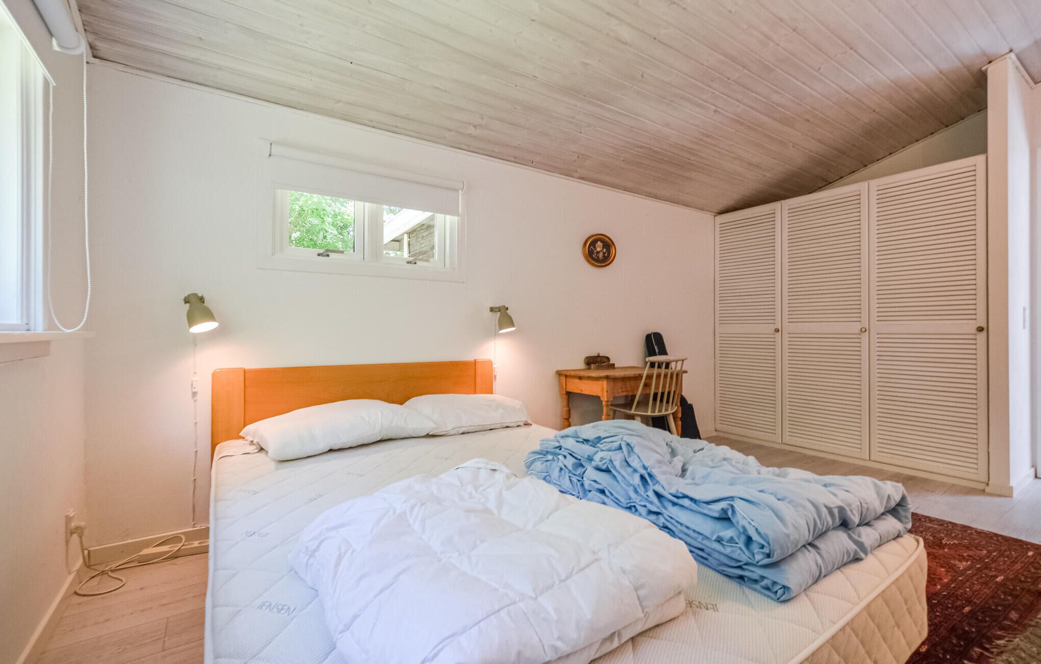 Une chambre à coucher comprenant un lit, deux lampes de chevet, une fenêtre, un bureau et une armoire.