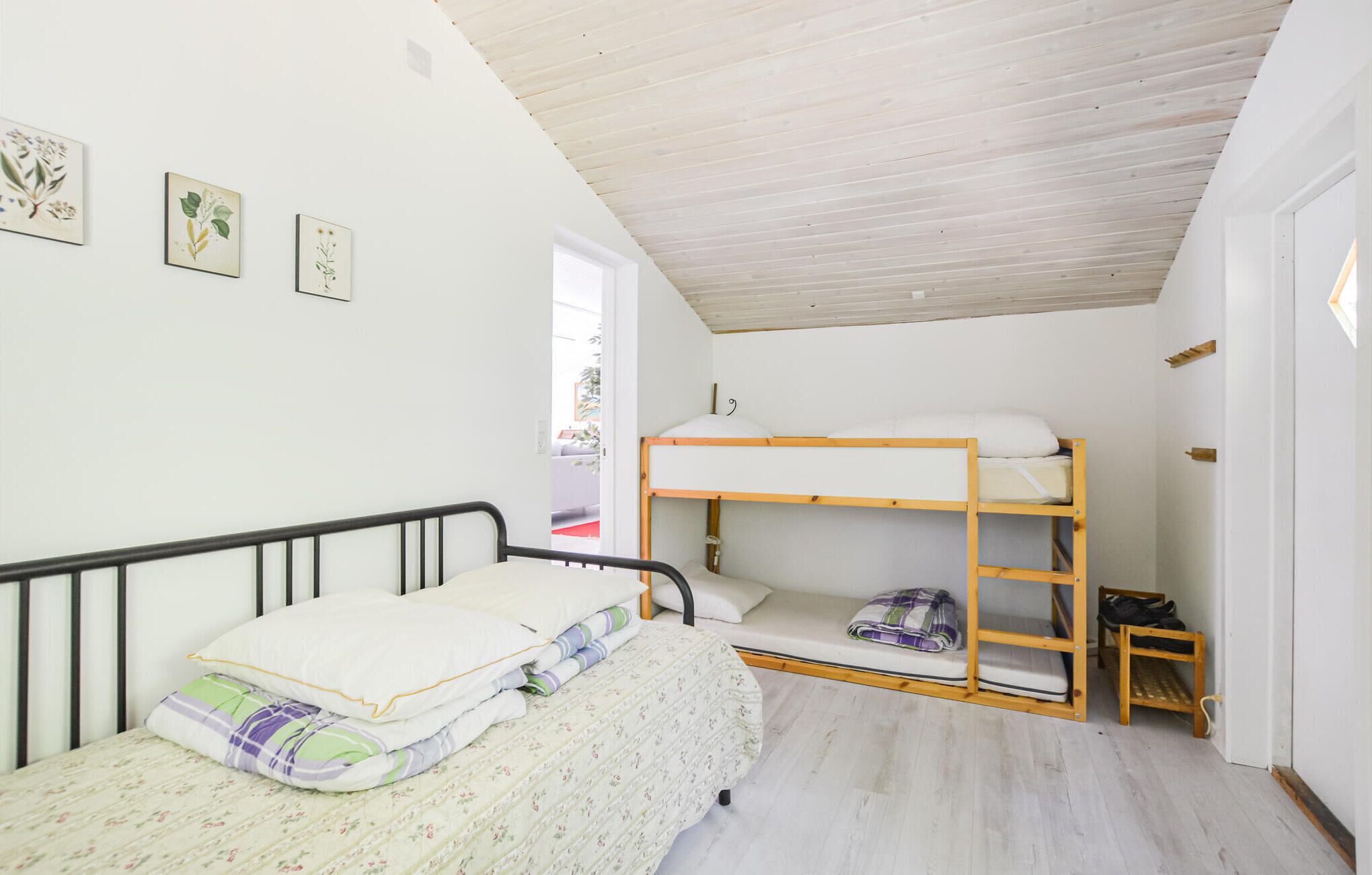 A small, well-lit room with a bunk bed, a single bed, and a door leading to another room.