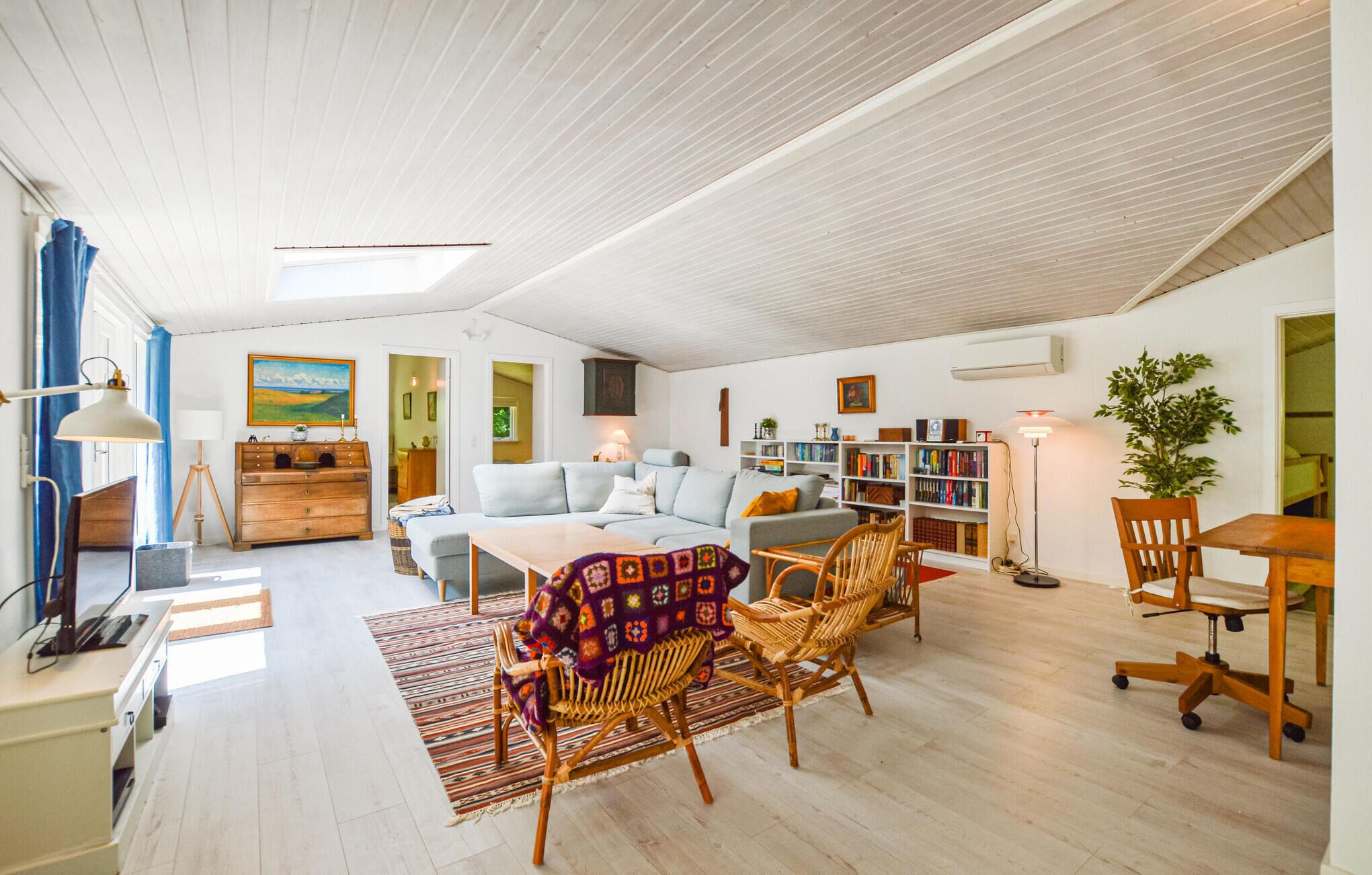 Een ruime woonkamer met een hoge plafond, een zithoek, een salontafel, een boekenkast en een eethoek met stoelen.