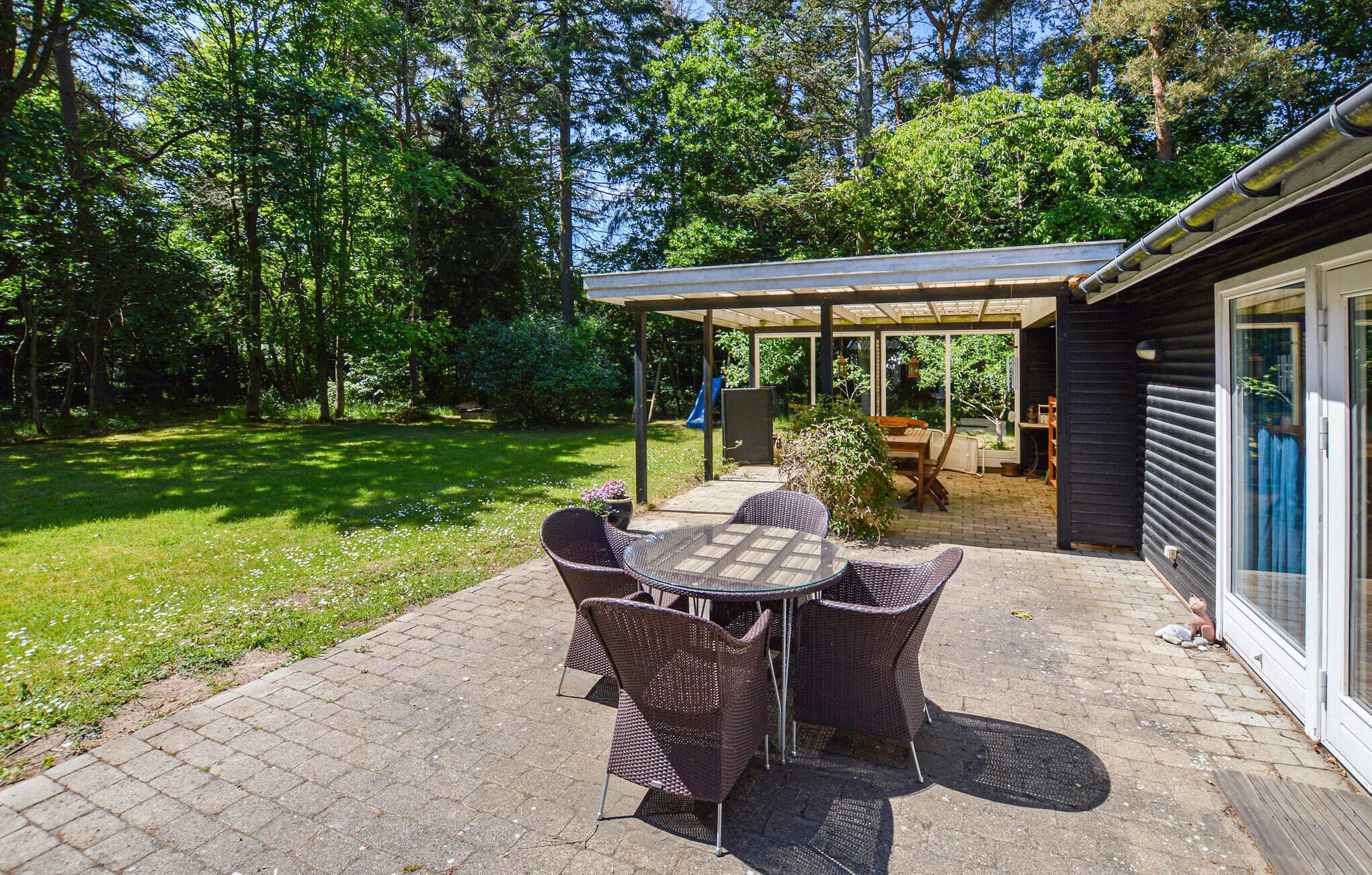A covered patio with a table and chairs, surrounded by a lush garden and a wooden deck.