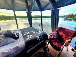 A cabin with a bed, a chair, and a view of a lake. - Overwater Hut Kuusamo (Kuusamo)