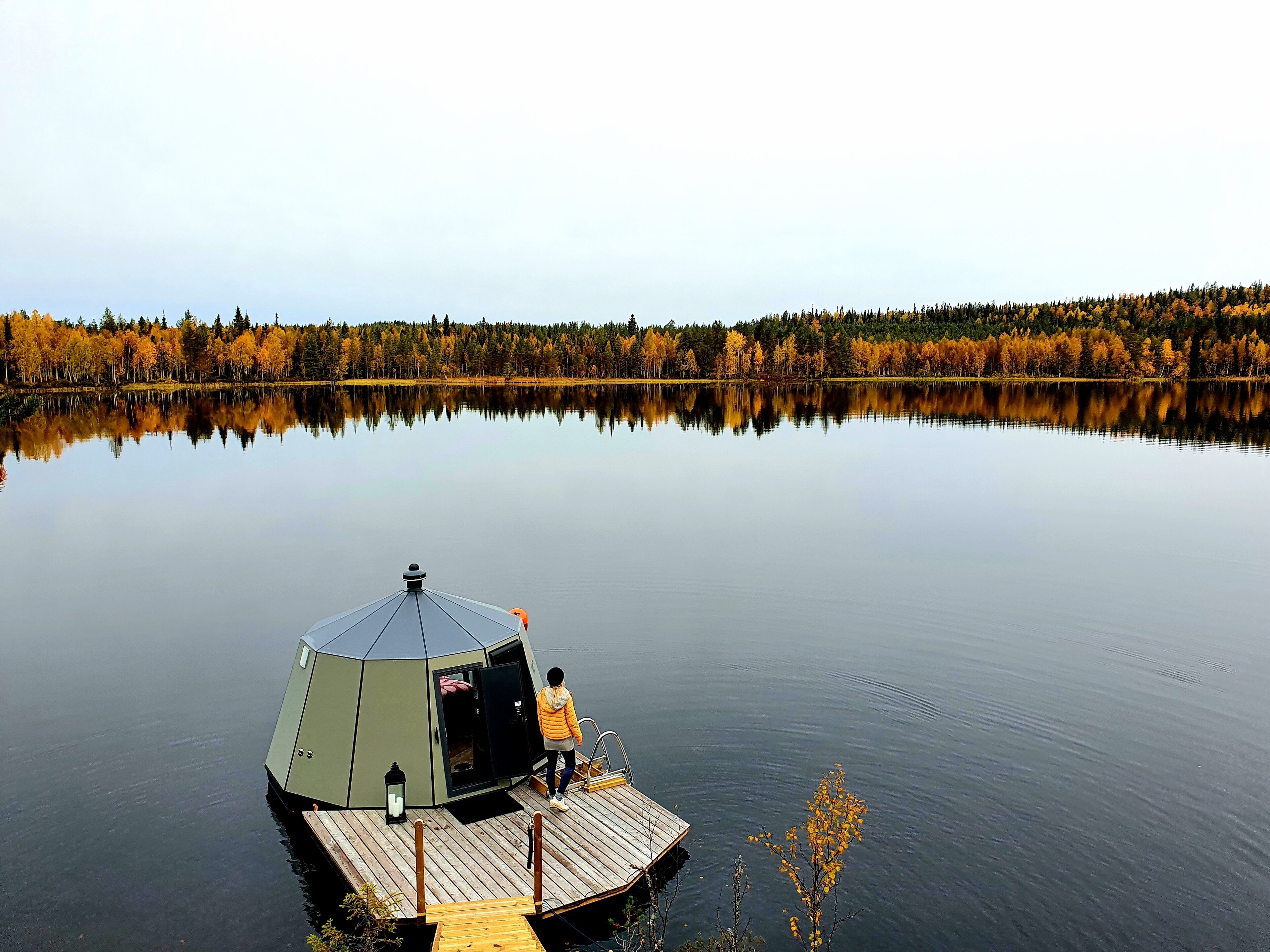 A stationary yurt-style structure on a calm lake with a forested shoreline.