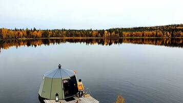A stationary yurt-style structure on a calm lake with a forested shoreline.