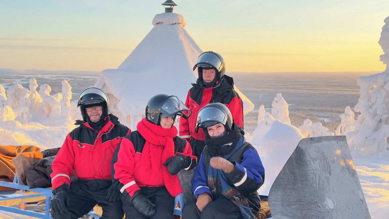 Un groupe de personnes se trouve au sommet d’une montagne enneigée, sous un ciel dégagé.