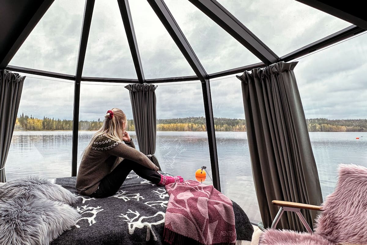 A cozy cabin with a large window overlooking a lake, a plush fur rug, and a chair with a pink throw.