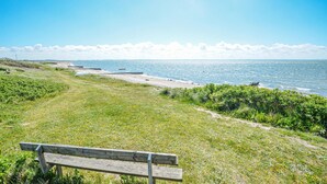 Un banc placé face à un sentier côtier, offrant une vue sur la mer et sur la terre au loin.