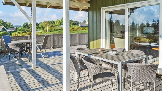 Une terrasse extérieure couverte, dotée d’une table et de chaises, d’une clôture en bois et offrant une vue sur le paysage environnant.