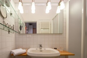 Ein Badezimmer mit einem weißen Waschbecken, einem Spiegel und einer Glasablage.