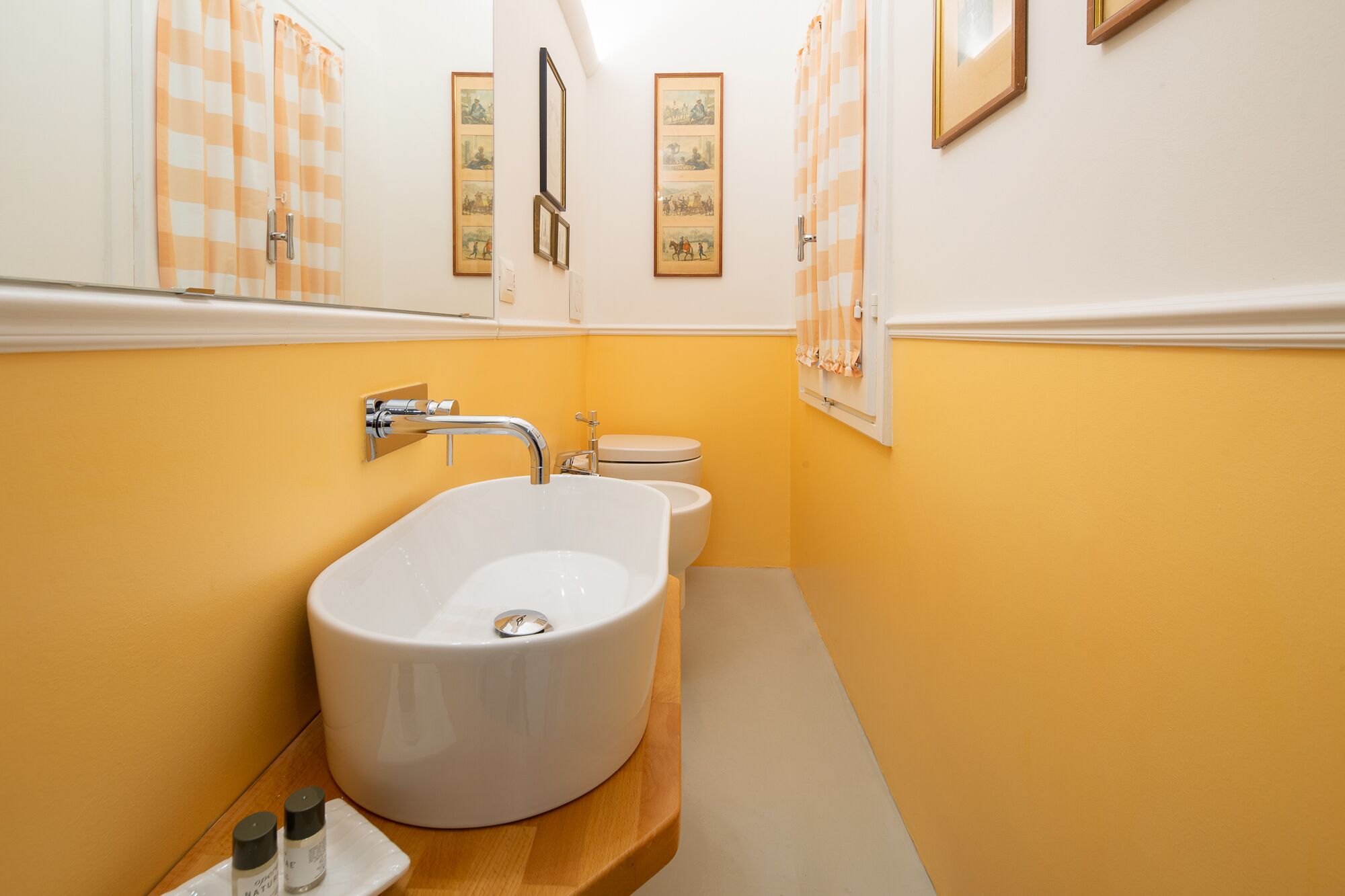 A bathroom with a large white bathtub, a white toilet, and a sink. The walls are painted yellow, and there are framed pictures on the wall.