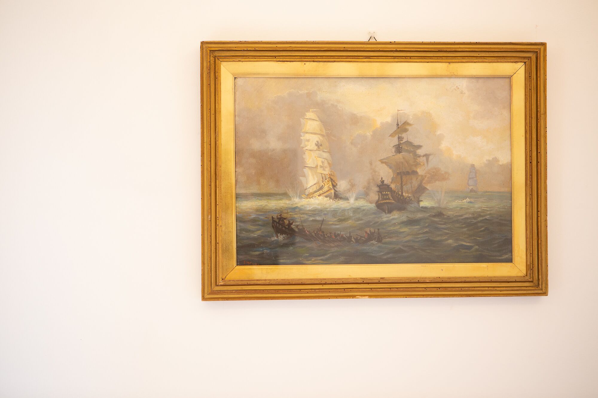 A framed painting of a shipwreck scene with a lighthouse in the background.