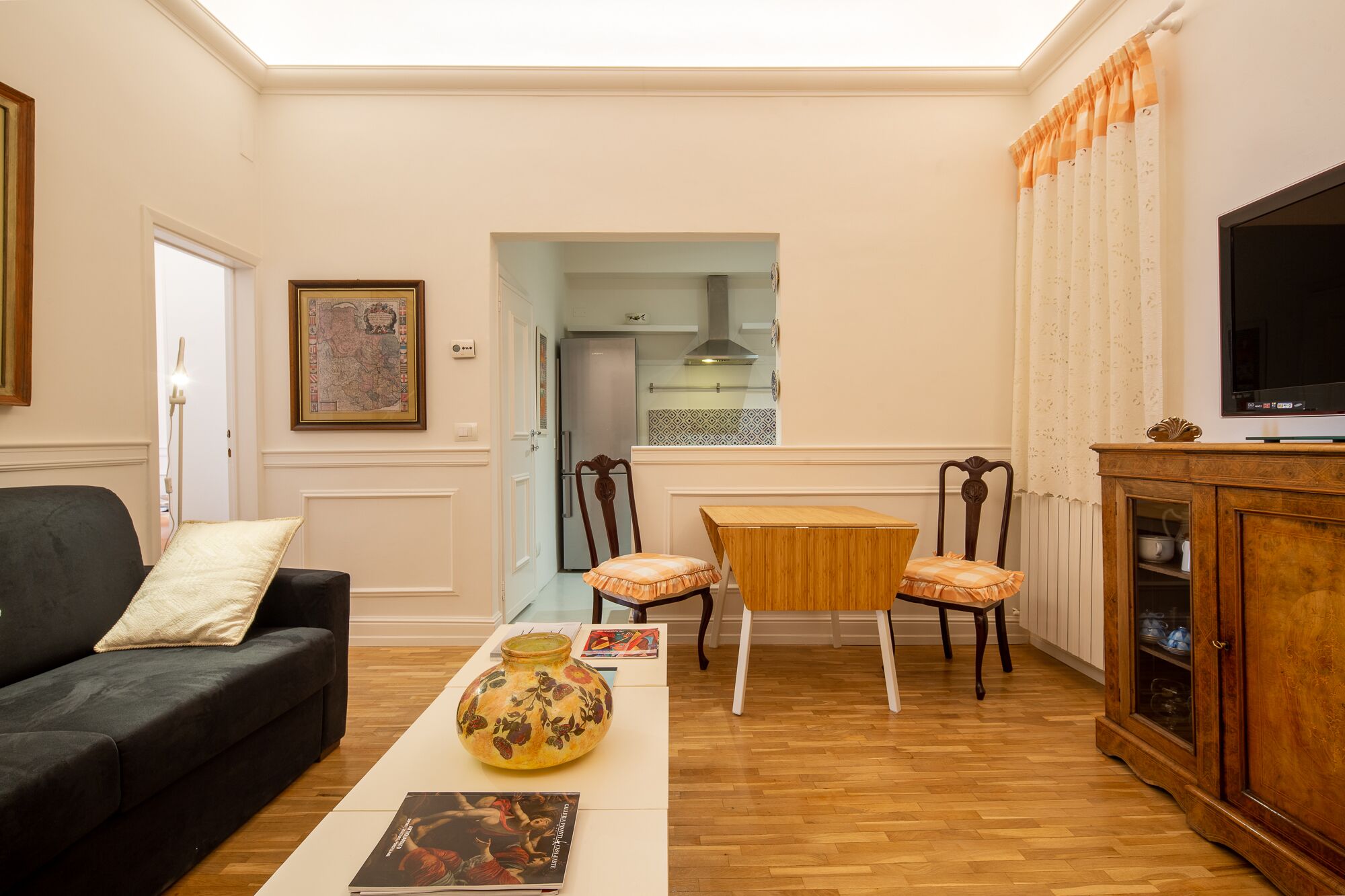 A living room with a sofa, a coffee table with a vase, two chairs, a TV, and a cabinet.