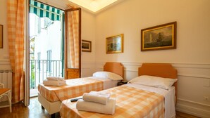 Habitación de hotel con dos camas, ropa de cama a cuadros, un cuadro y un balcón con vistas.