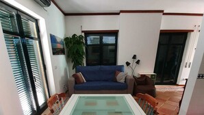 Un comedor con una mesa de vidrio rodeada de sillas de madera, un sofá azul y una planta en maceta.