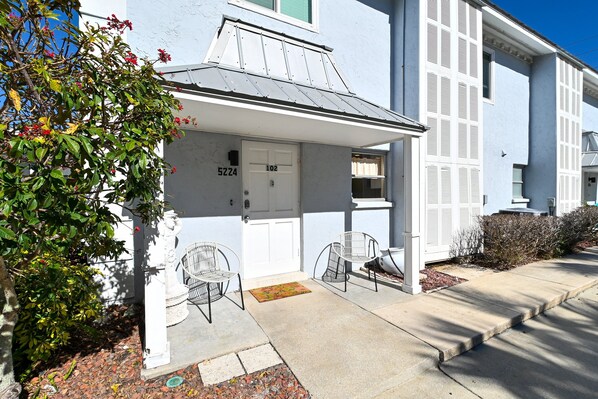 A residential building with a white facade, a number "5224" on the door, and a small porch with two chairs.