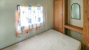 A small, simple room with a single bed, a window with a curtain, and a mirror on the wall.