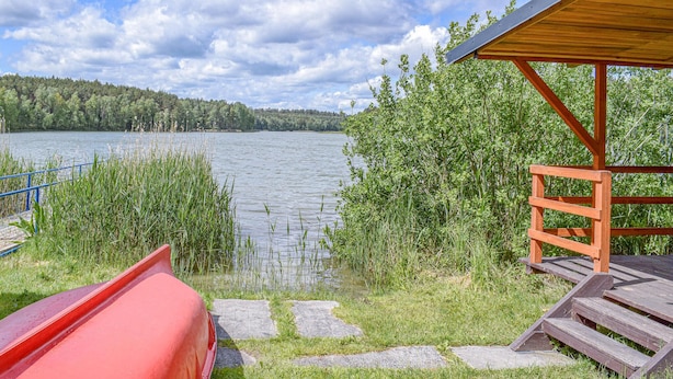 A lakeside deck with a red canoe, a wooden shelter, and a stone pathway leading to the water.