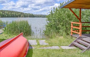 Una terraza junto al lago con un canoa roja, un refugio de madera y un camino de piedra que lleva al agua.