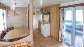 A caravan interior with a kitchenette, a sleeping area, and a sliding glass door to the outside.