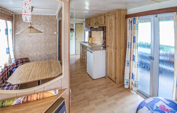 Interior de una caravana con kitchenette, zona de descanso y puerta corrediza de vidrio hacia el exterior.