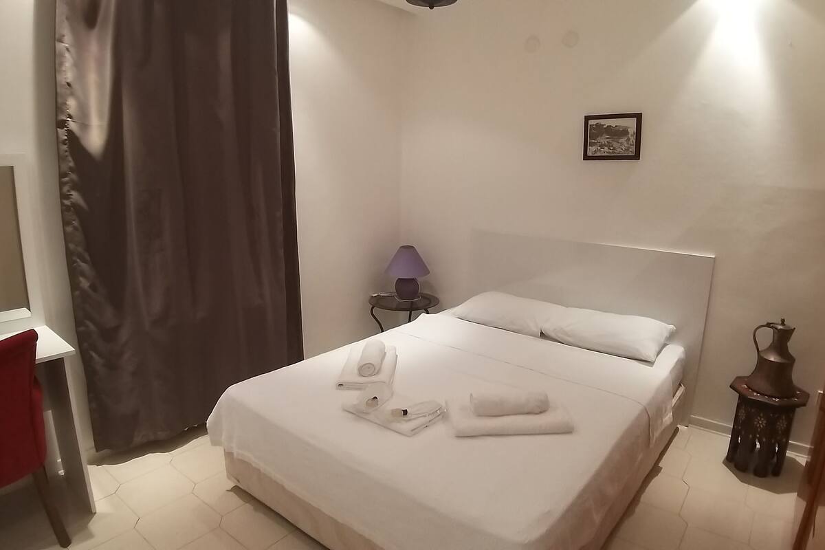 A neatly made bed with white linens and towels, a small bedside table with a lamp, and a picture on the wall.