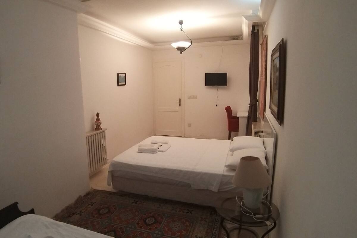 A small, neatly arranged bedroom with a bed, a bedside lamp, a radiator, and a small table.