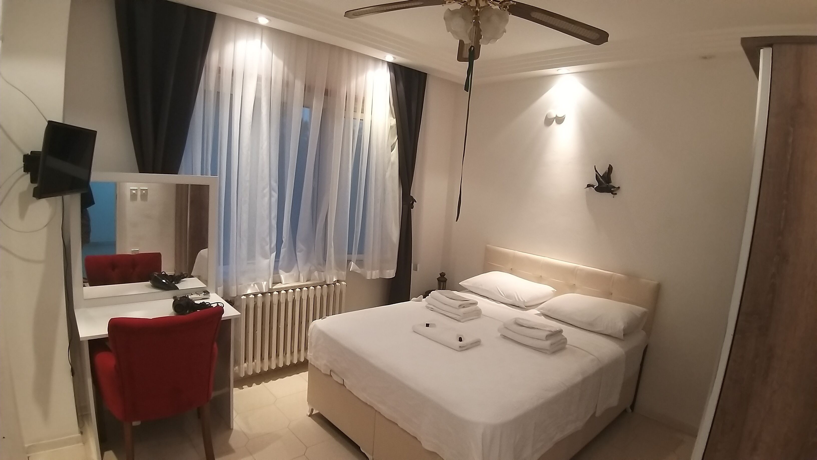 Una habitación de hotel con cama, un escritorio con silla, un espejo y un ventilador de techo.