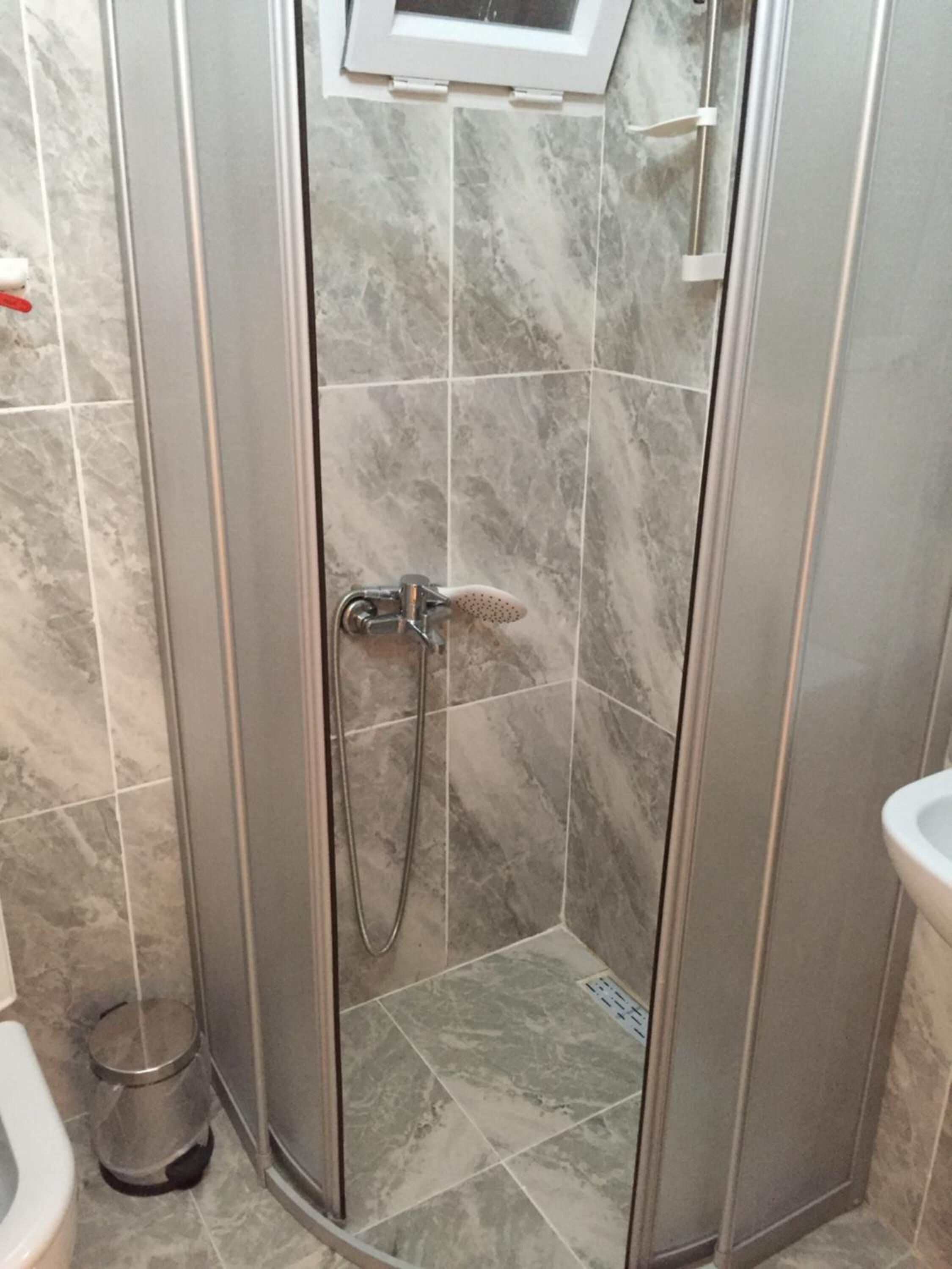 A modern bathroom with a glass-enclosed shower, marble tiles, and a visible toilet.
