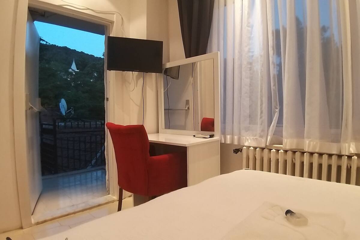 A hotel room with a bed, a desk with a chair, a TV, and a window with curtains.