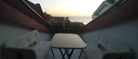 Un pequeño balcón con una mesa y dos sillas, con vistas a una zona residencial al atardecer.