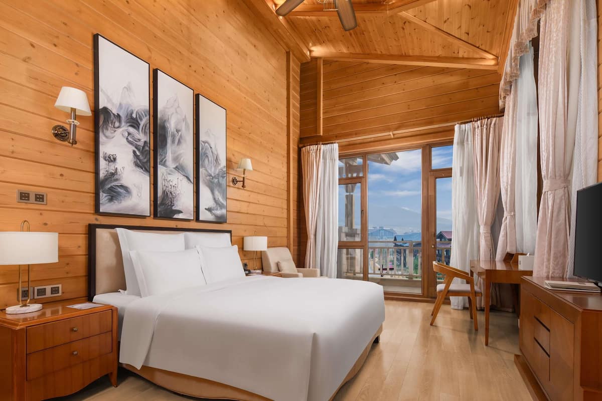 A wooden room with a bed, bedside tables, a desk, and a TV.