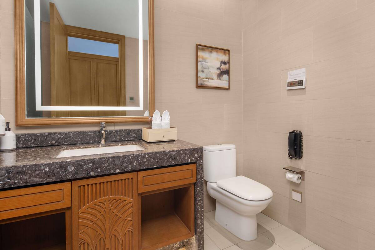 A bathroom with a large mirror, a sink, a toilet, and a shower area.